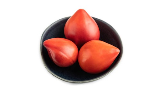 Red Heart shape tomatoes in blue bowl isolated on white background. Side view, copy space, flat lay