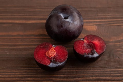 Purple Plum Cut in half on brown wooden background. Side view, close up. healthy food, vegetable,