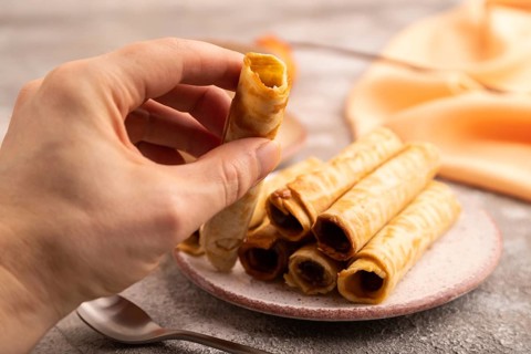 Waffles with caramel with hand on brown concrete background and orange linen textile, side view,