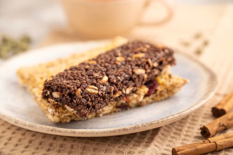 Granola bars with caramel, nuts, flakes in ceramic plate on brown concrete background, beige linen