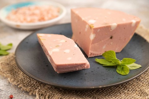Mortadella sausage on plate with pepper and herbs on brown concrete background and linen textile.