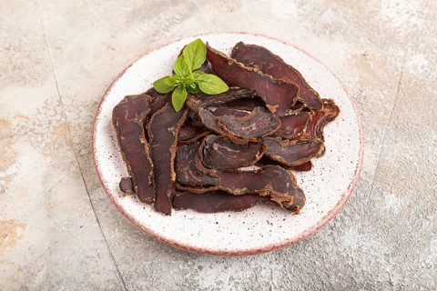 Armenian Basturma dried meat on plate with pepper and herbs on brown concrete background. Side