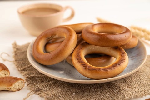Homemade Ring Bagel with cup of coffee on white wooden background and linen textile. side view,