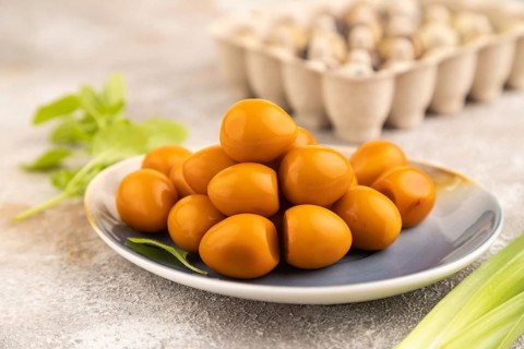 Pile of Smoked Quail eggs on plate on a brown concrete background. side view, close up, selective