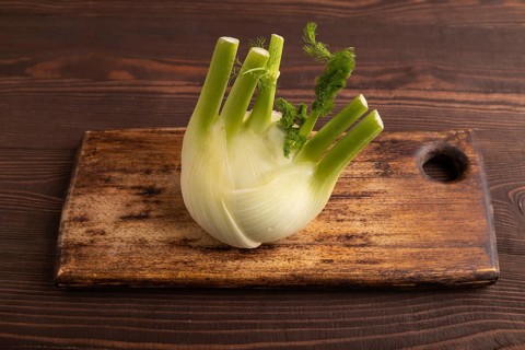 Fresh Fennel bulb on wooden cutting board on brown wooden background, side view, close up,
