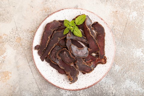 Armenian Basturma dried meat on plate with pepper and herbs on brown concrete background. Top view,