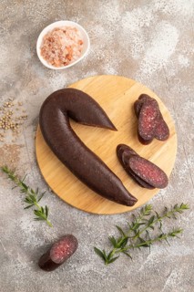 Sujuk sausage on wooden cutting board with pepper and herbs on brown concrete background. Top view,