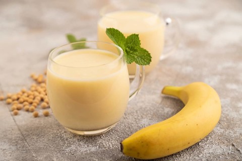 Organic non dairy banana and soy milk in glass on brown concrete background. Vegan healthy food