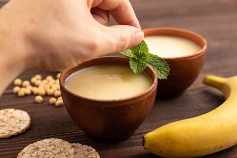 Organic non dairy banana and soy milk in clay cup with hand on brown wooden background. Vegan