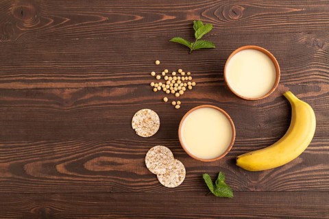 Organic non dairy banana and soy milk in clay cup on brown wooden background. Vegan healthy food