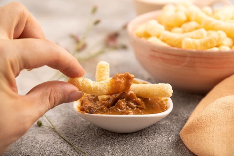 Corn flakes sticks with hand with caramel in ceramic bowl on gray concrete background and orange