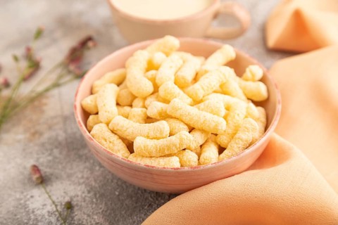 Corn flakes sticks with caramel in ceramic bowl on gray concrete background and orange linen