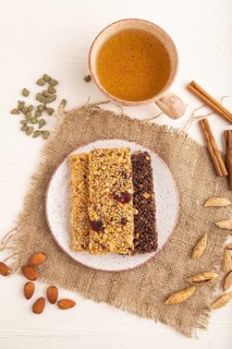 Granola bars with caramel, nuts, flakes in ceramic plate on white wooden background, beige linen