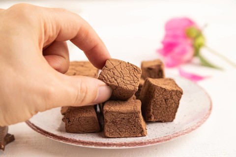 Chocolate marshmallow with cup of coffee with hand on white wooden background. side view, close up,
