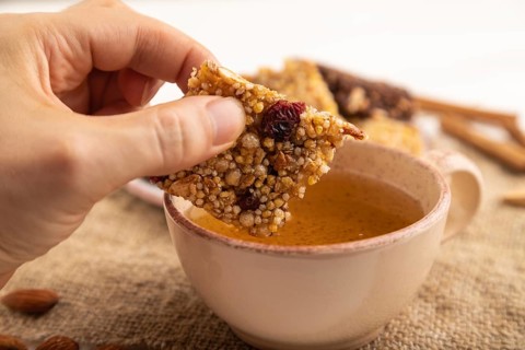 Granola bars with caramel, nuts, flakes in ceramic plate with hand on white wooden background,
