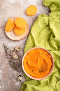 Sweet potato porridge in ceramic bowl on brown concrete background and green textile. Diet, healthy
