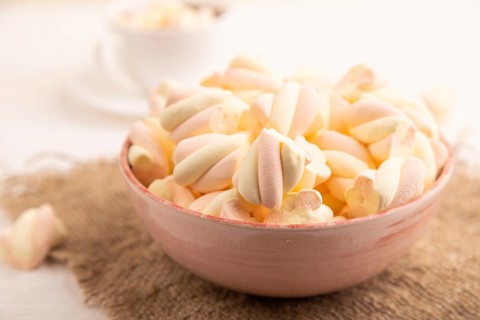 Orange and pink marshmallow in ceramic bowl on white wooden background, side view, close up,