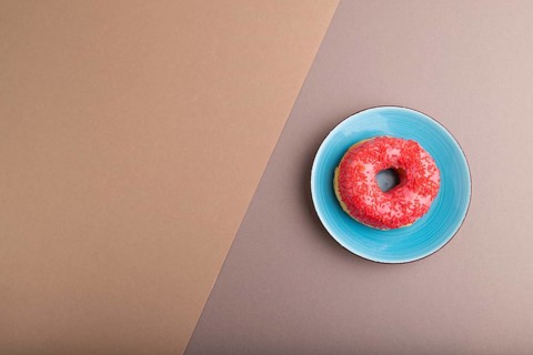 Pink Donut with sprinkles on blue ceramic plate on beige and gray pastel paper background, top