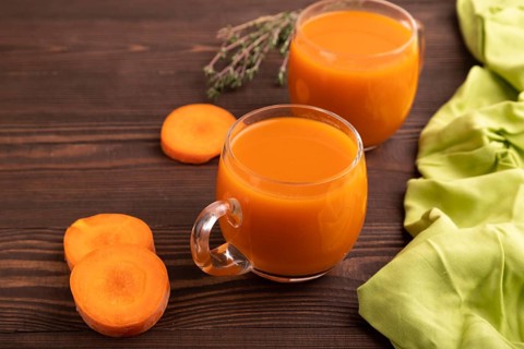Two glasses with carrot juice, on wooden background and green textile. Diet, healthy eating concept