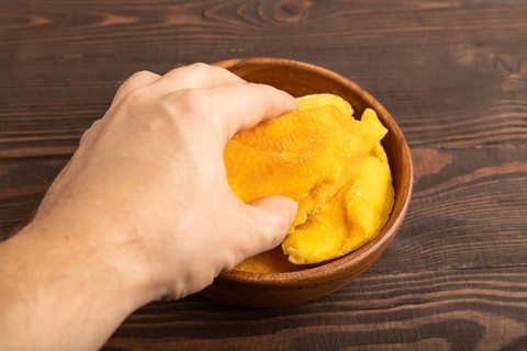 Dried Mango in wooden bowl with hand on brown wooden background. Side view, close up. healthy food,