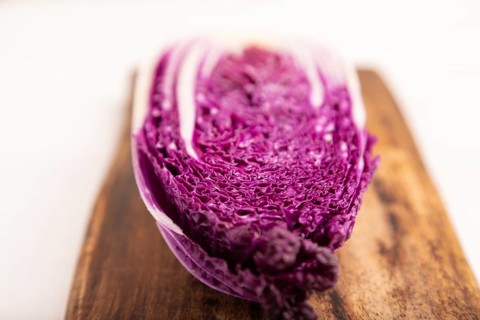 Purple Chinese cabbage on cutting board on white wooden background, top view, flat lay, close up,