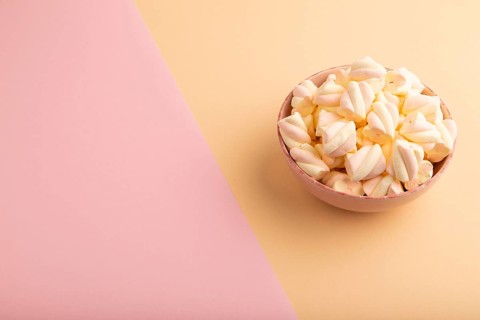 Orange and pink marshmallow in ceramic bowl on pink and orange pastel paper background, side view,