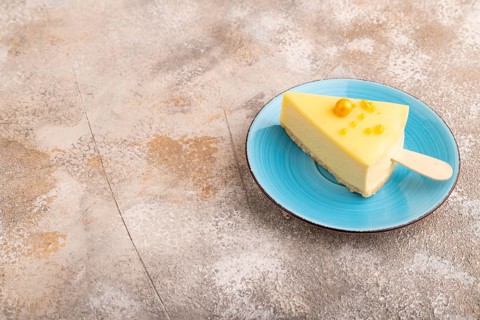 Yellow Cake pop with sprinkles on blue ceramic plate on brown concrete background, side view, copy