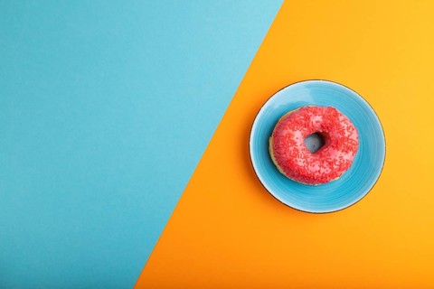 Pink Donut with sprinkles on blue ceramic plate on blue and orange pastel paper background, top
