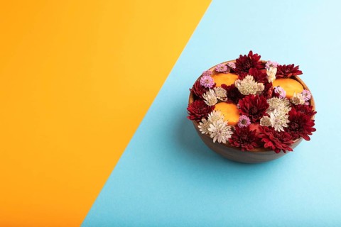 Wooden bowl with carrot slices and red Chrysanthemum flowers, Astrantia flowers, flower salad on