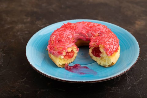 Bitten Pink Donut with sprinkles on blue ceramic plate on black concrete background, side view,