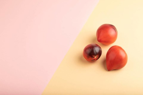 Red Heart shape tomatoes on pink and orange pastel paper background. Side view, copy space. healthy