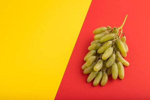 Green grapes on yellow and red paper pastel background. Side view, copy space. healthy food,