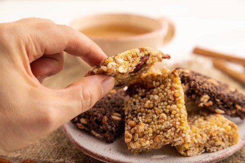 Granola bars with caramel, nuts, flakes in ceramic plate with hand on white wooden background,
