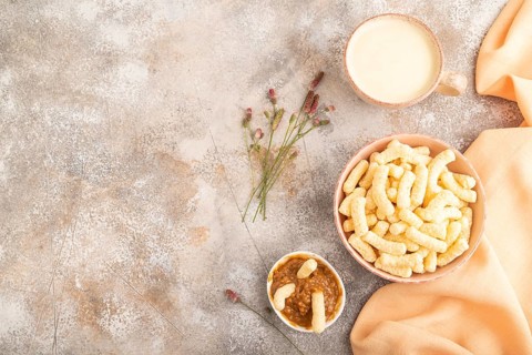 Corn flakes sticks with caramel in ceramic bowl on gray concrete background and orange linen