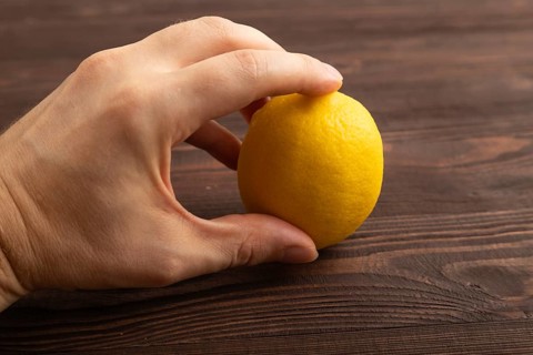 Yellow Lemon Cut in half with hand on brown wooden background. Side view, close up. healthy food,
