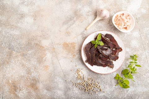 Armenian Basturma dried meat on plate with pepper and herbs on brown concrete background. Top view,