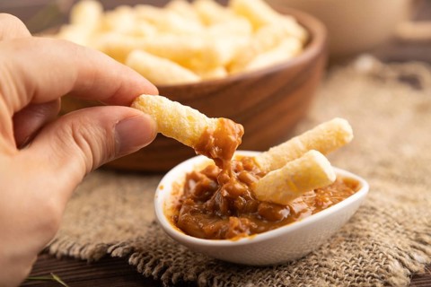 Corn flakes sticks with caramel in wooden bowl with hand on brown wooden background and linen