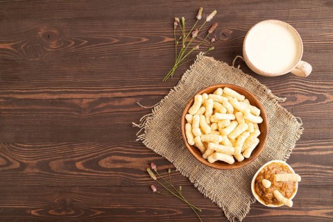 Corn flakes sticks with caramel in wooden bowl on brown wooden background and linen textile. Top