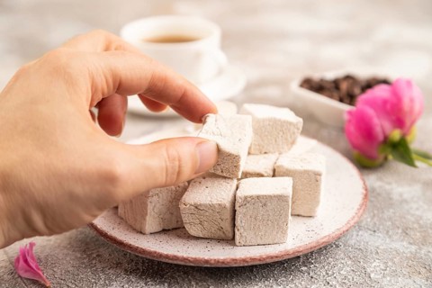 Coffee marshmallow with cup of coffee with hand on brown concrete background. side view, close up,