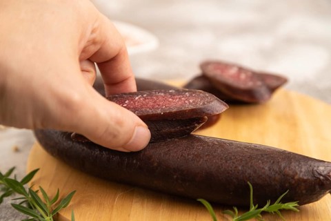 Sujuk sausage with hand on wooden cutting board with pepper and herbs on brown concrete background.