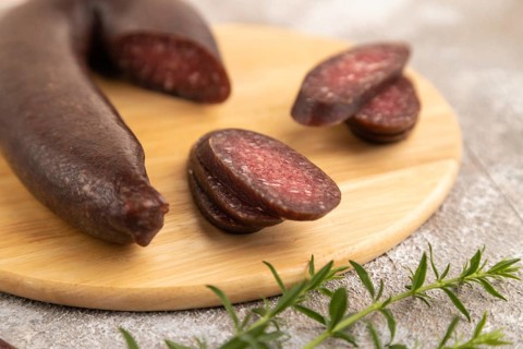 Sujuk sausage on wooden cutting board with pepper and herbs on brown concrete background. Side