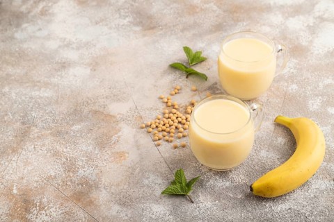 Organic non dairy banana and soy milk in glass on brown concrete background. Vegan healthy food