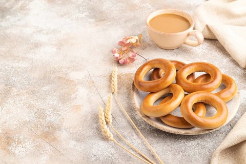 Homemade Ring Bagel with cup of coffee on brown concrete background and linen textile. side view,