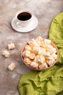 Orange and pink marshmallow in ceramic bowl on brown concrete background and green textile, side