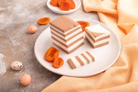 Cocoa and milk jelly with dried apricots on brown concrete background and orange textile, side
