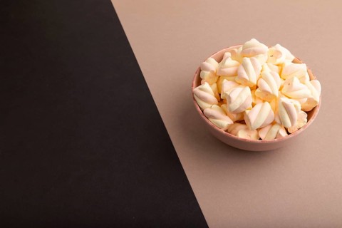 Orange and pink marshmallow in ceramic bowl on black and beige pastel paper background, side view,