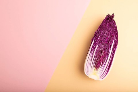 Purple Chinese cabbage on pink and orange pastel paper background, top view, flat lay, copy space,