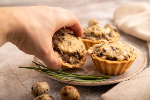 Tartlets with meat and cheese with hand on brown concrete background and linen textile. side view,