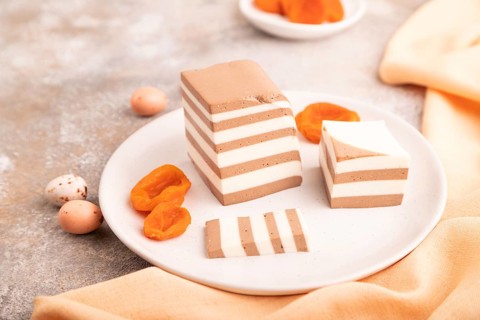 Cocoa and milk jelly with dried apricots on brown concrete background and orange textile, side