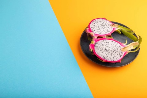 Ripe Pitaya on blue plate on blue and orange pastel paper background, side view, copy space,